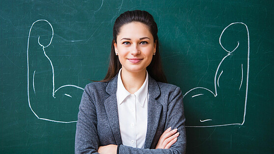 Female professorin in front of blackboard, drawing showing flexed muscled arms in background; Brain City Berlin 