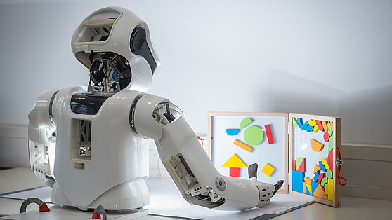 Humanoider Roboter vor einer Tafel mit geometrischen Elementen