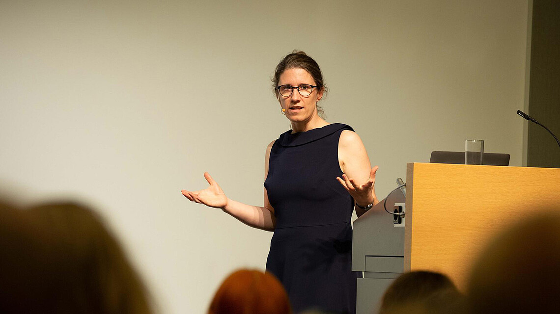 Dr. Barbara Vetter, professor of theoretical philosophy at the FU Berlin, gives a lecture. She wears a black dress and gestures toward the audience; Brain City Berlin 