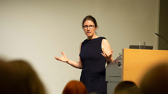 Prof. Dr. Barbara Vetter, Professorin für Theoretische Philosophie an der FU Berlin hält einen Vortrag. Sie trägt ein schwarzes Kleid und gestikuliert in Richtung Publikum, Brain City Berlin.