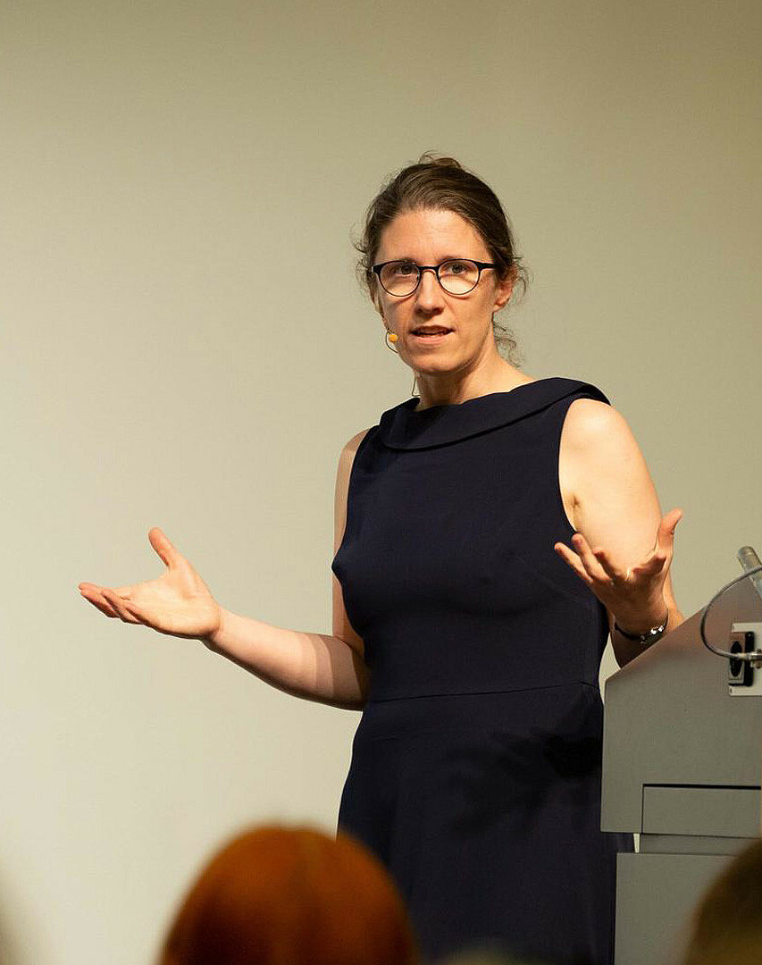 Prof. Dr. Barbara Vetter, Professorin für Theoretische Philosophie an der FU Berlin hält einen Vortrag. Sie trägt ein schwarzes Kleid und gestikuliert in Richtung Publikum, Brain City Berlin.