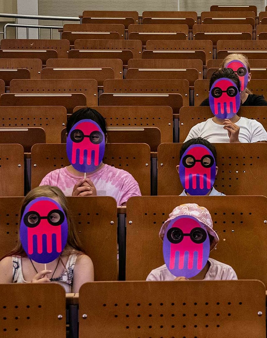 Kinder mit KUL-Masken im Hörsaal. 